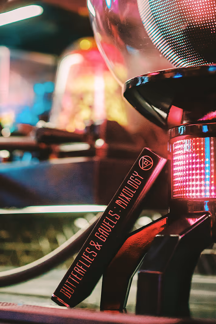 Close-up of a book titled 'Butterflies & Gavels: Mixology' next to a glowing futuristic device.