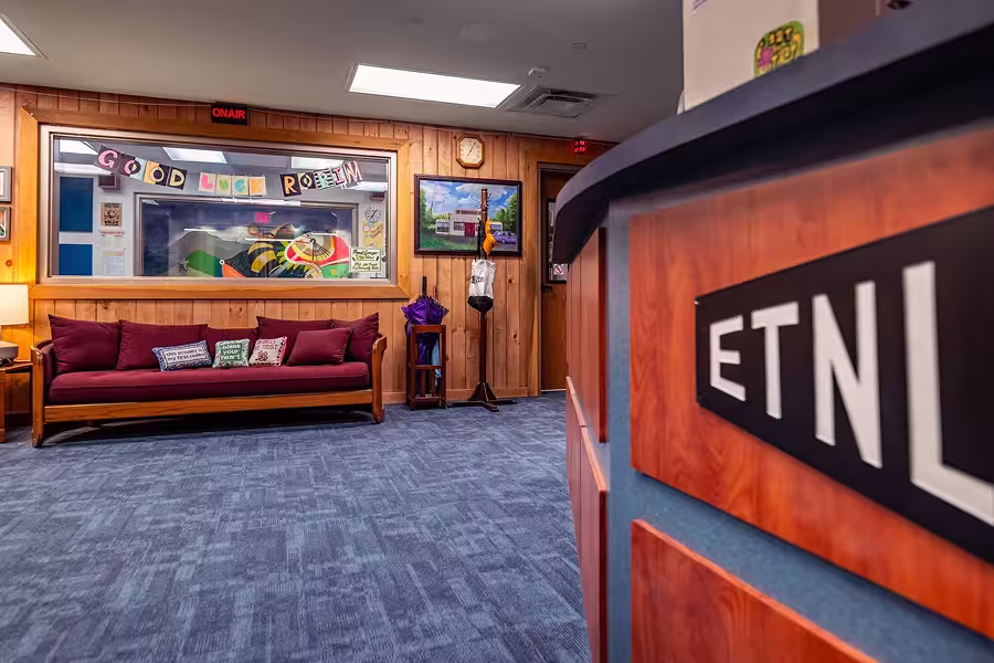 Radio station lobby with wooden walls, purple couch, 'Good Luck Robin' banner, and ETNL sign on desk.
