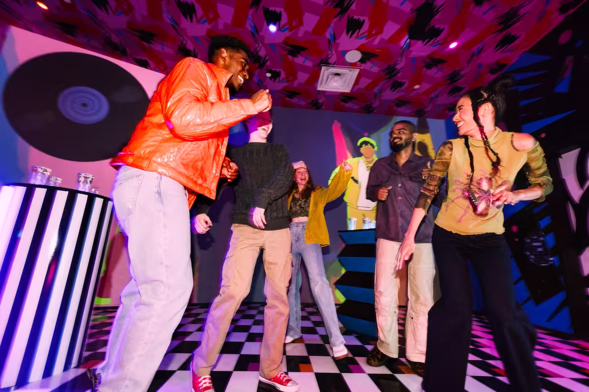people dancing and smiling inside a space with a black and white checkered floor and a record hanging on the wall